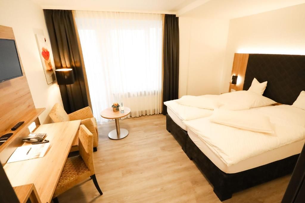 A hotel room with a bed, a desk, a chair, a small table, and a TV.