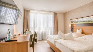 Ein Hotelzimmer mit einem Bett, einem Schreibtisch mit Stuhl, einem Fernseher und einem Fenster mit Vorhängen.