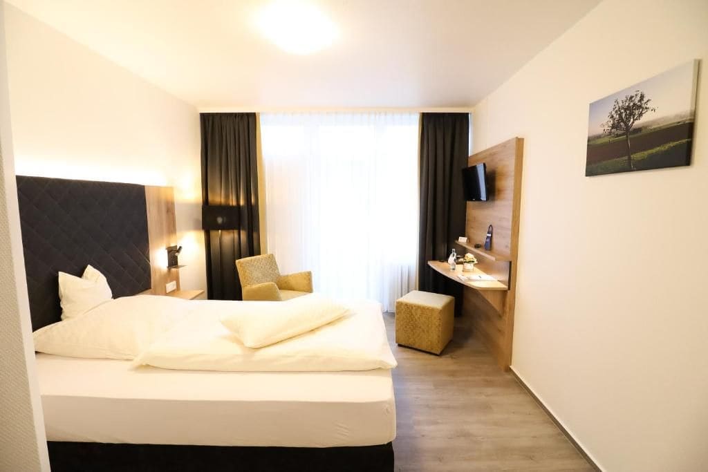 Een hotelkamer met een bed, een bureau, een stoel, een televisie en een schilderij aan de muur.