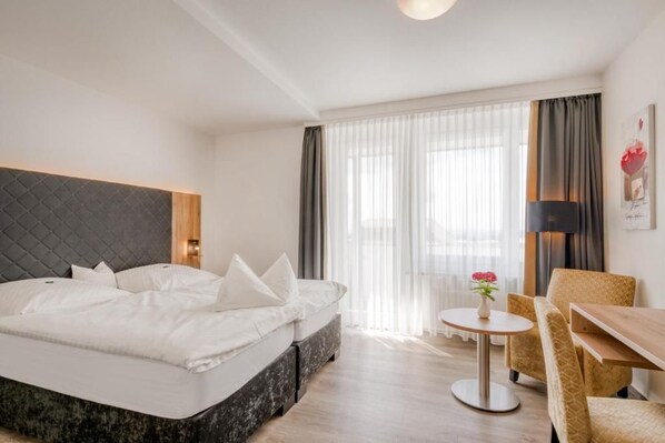 A hotel room with a bed, a round table, a chair, and a window with curtains.