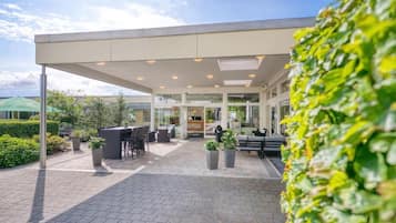 An outdoor seating area with tables and chairs, a covered walkway, and potted plants.