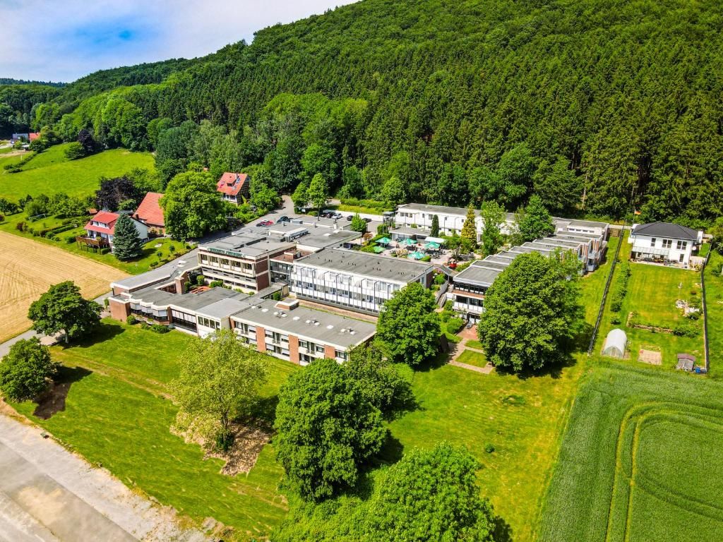 Vista aérea de un campus con varios edificios, campos verdes y una colina boscosa al fondo.