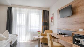 Une chambre d’hôtel comprenant un lit, une table ronde, deux chaises, un bureau avec un téléphone, un téléviseur à écran plat fixé au mur et une fenêtre avec des rideaux légers.