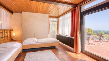 A bedroom with a wooden ceiling, a brick wall, a large window, and a view of the outdoors.