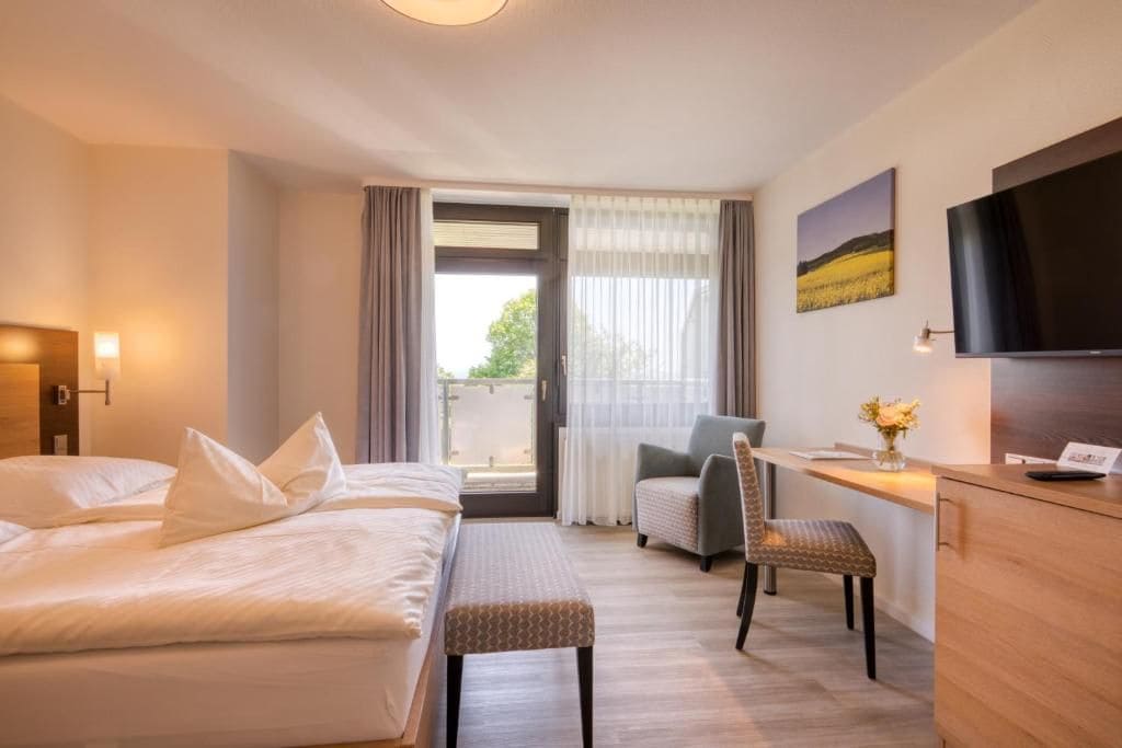 Una habitación de hotel con cama, escritorio con silla, televisor y ventana con cortinas.