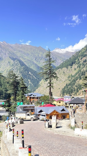 A mountainous landscape with a clear sky, a parking area with vehicles, and buildings with red roofs.