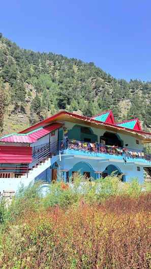 A multi-story building with a balcony, surrounded by vegetation.