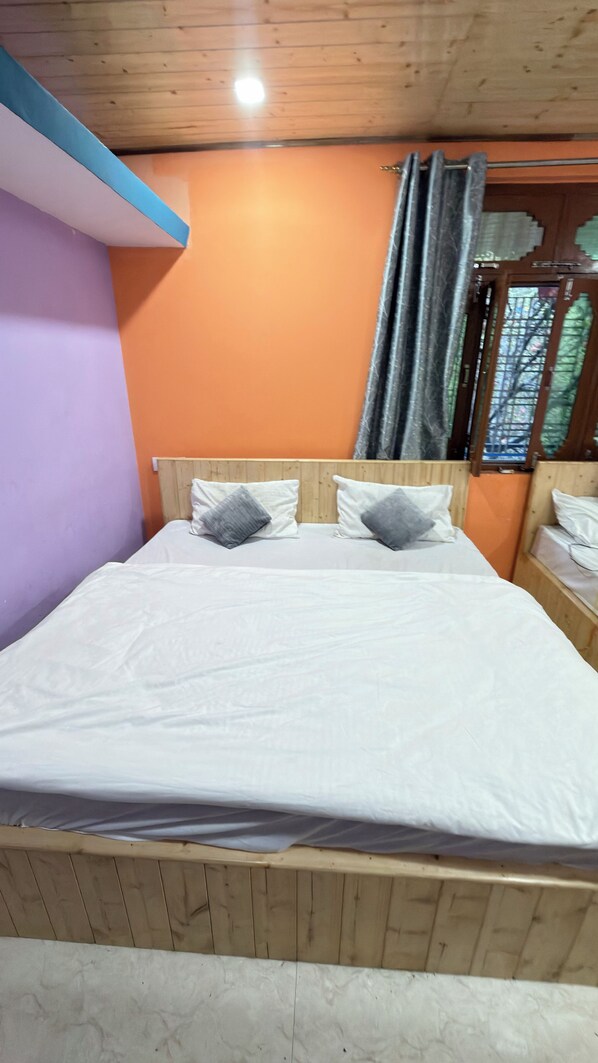 A room with a wooden bed, two pillows, a wooden headboard, an orange wall, and a window with curtains.