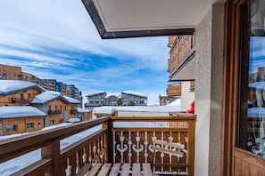 A balcony with a wooden railing overlooking a snow-covered town with various buildings. - Val Thorens: Cozy Apartment in the Heart of the Resort (Les Belleville)