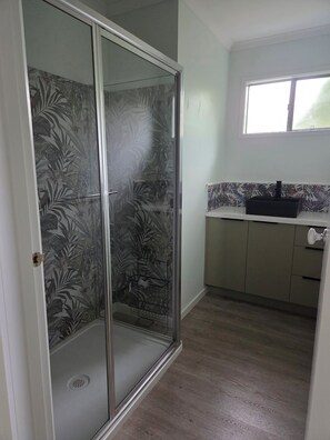 A room with a sliding glass door leading to a shower area with a leaf-patterned glass door. There is a sink with a black faucet on the countertop, and the room has a tiled backsplash. - Holiday Rental Red Rocks Area Phillip Island (Cowes)