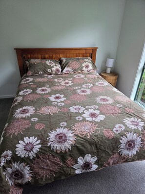 A bed with a floral bedspread, a wooden headboard, a bedside lamp, and a window with a view. - Holiday Rental Red Rocks Area Phillip Island (Cowes)