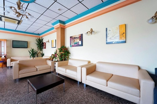 Un vestíbulo con tres sofás color beige, una mesa de centro negra y un televisor en la pared.