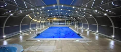 An indoor swimming pool with a tiled floor, surrounded by a curved ceiling structure with lighting fixtures.