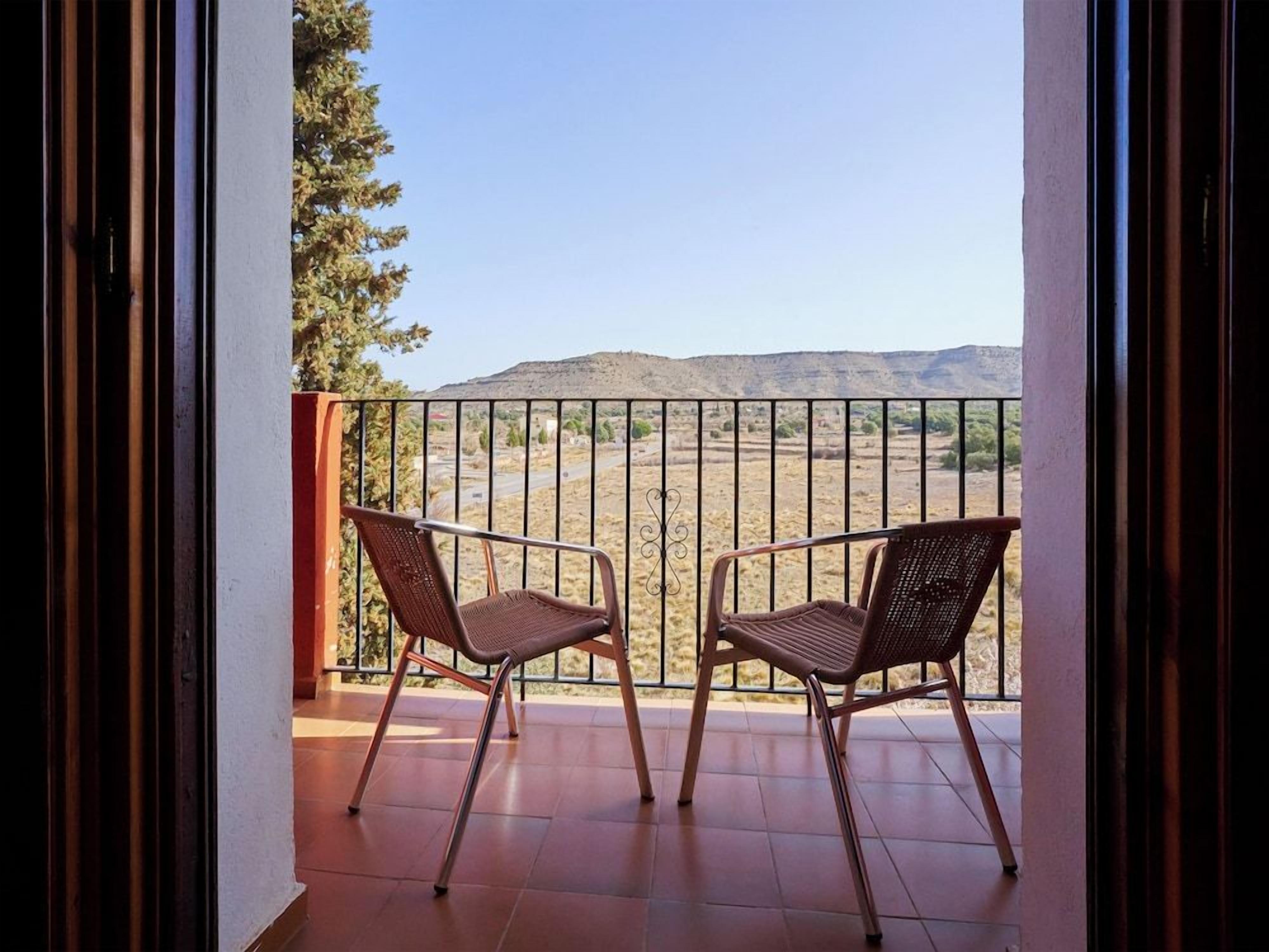 A balcony with two wicker chairs, a metal railing, and a view of a desert landscape.