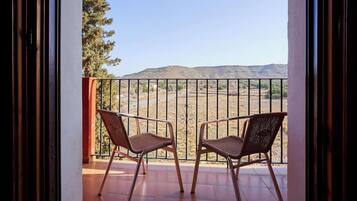 A balcony with two wicker chairs, a metal railing, and a view of a desert landscape.