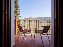 Un balcón con dos sillas de mimbre, baranda de metal y vista a un paisaje desértico.