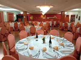 Un salón de banquetes con mesas redondas dispuestas para el servicio de comidas, cada una con mantel blanco, cubertería y cristalería.
