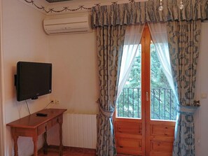 Una habitación con una televisión sobre una mesa de madera, una ventana con cortinas estampadas y vistas a zonas verdes.