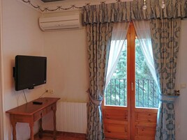 Una habitación con una televisión sobre una mesa de madera, una ventana con cortinas estampadas y vistas a zonas verdes.
