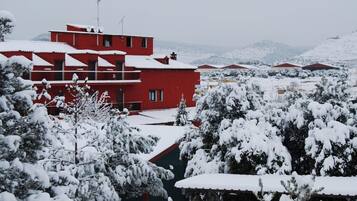A red building with multiple windows and balconies, surrounded by snow-covered trees and hills in the background.