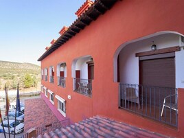 Un edificio con fachada roja, varios balcones y una puerta con persiana cerrada.