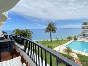 A balcony with a view of a swimming pool, palm trees, and a building with multiple floors. - Apartment in Nerja Near Balcon de Europa (Nerja)