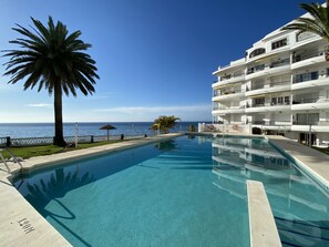 A swimming pool with a view of the ocean, surrounded by a white building with balconies. - Apartment in Nerja Near Balcon de Europa (Nerja)