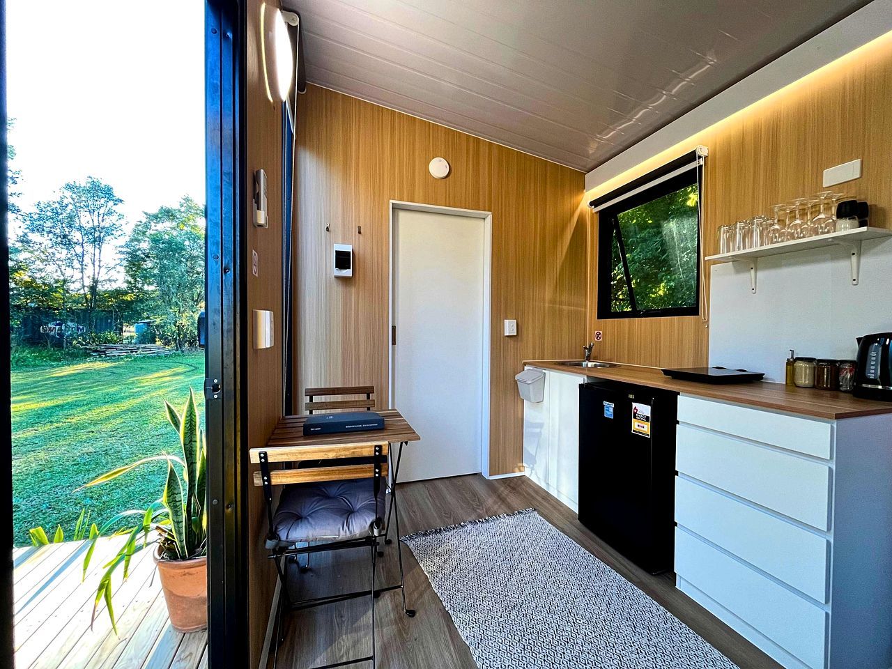 A compact kitchen with a dining area, a built-in TV, and a view of a green landscape.