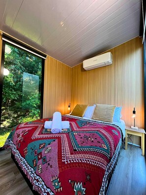 A modern bedroom with a large bed, a window, and a wall-mounted air conditioner. - Tranquil Tiny Cabin Retreat with Stargazing near Sunshine Coast, Yandina QLD (Nambour)