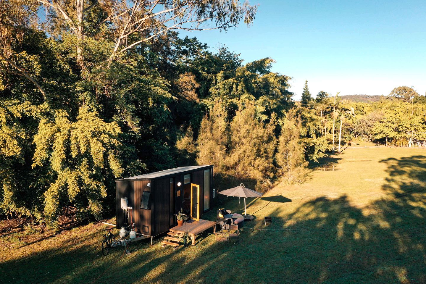 Une petite cabane avec une porte, un banc et une table avec des chaises à l’extérieur.
