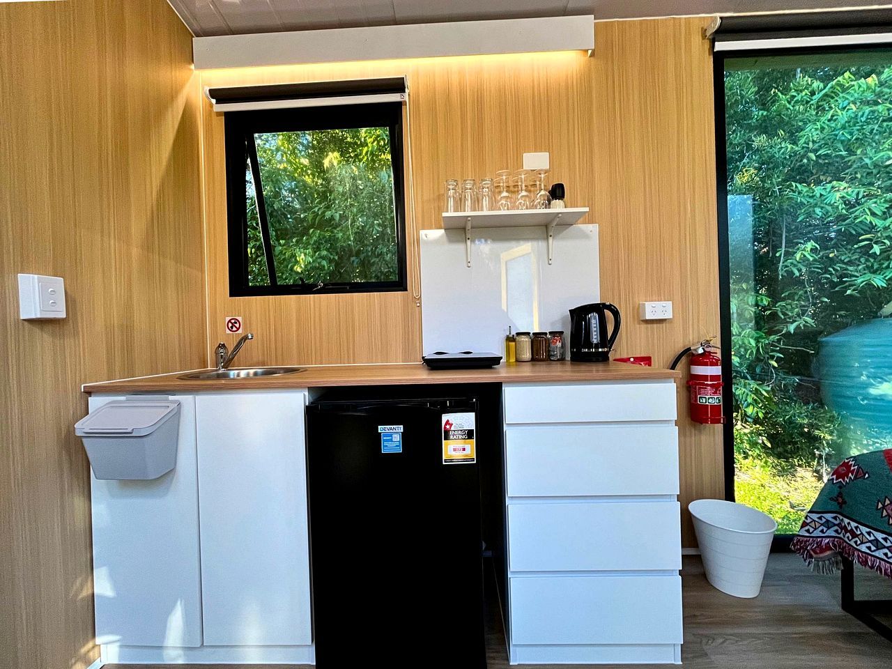 A compact kitchenette with a sink, a small refrigerator, a microwave, and a window with a view of greenery.
