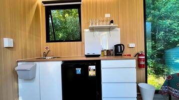 A compact kitchenette with a sink, a small refrigerator, a microwave, and a window with a view of greenery.