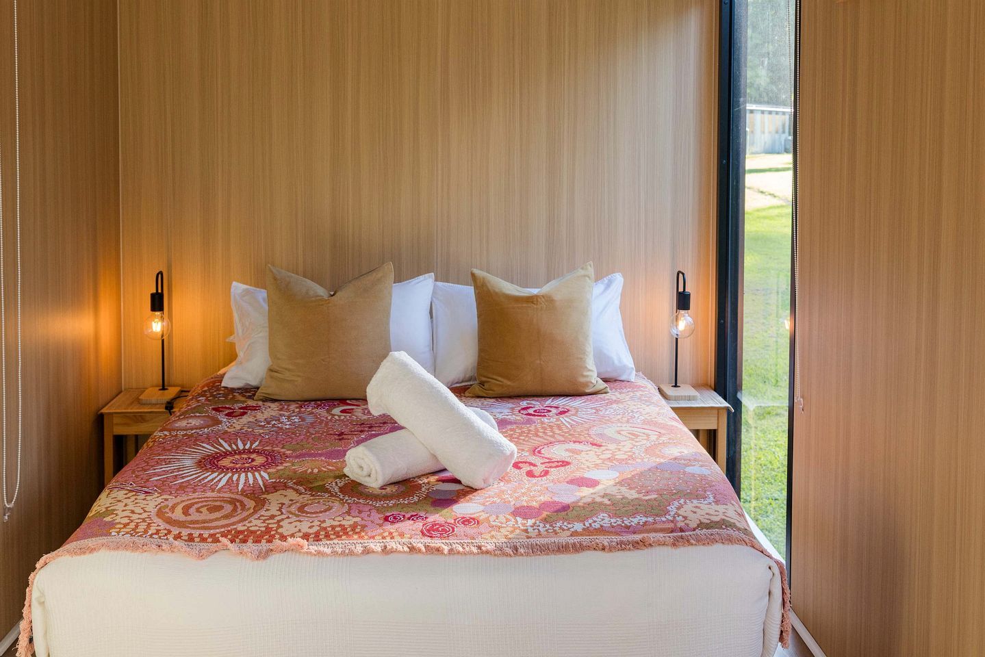 A hotel room with a bed, pillows, a rolled towel, and two bedside lamps.