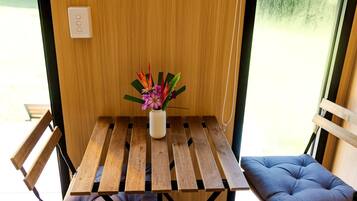 Een kleine houten tafel met een bloevas, twee comfortabele stoelen en een raam met uitzicht op groen.