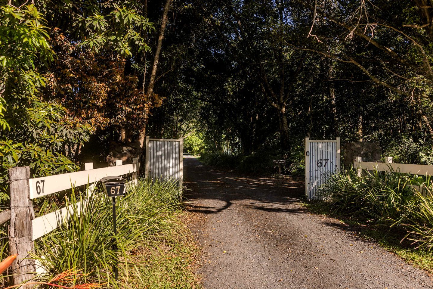Una carretera rural que conduce a una entrada con portón y un letrero con el número 67.