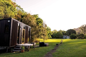 A modern, compact structure with a dining area and outdoor seating, surrounded by lush greenery and trees.