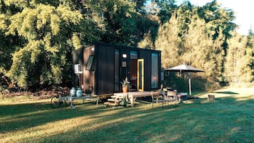 A small cabin with a deck, surrounded by trees.