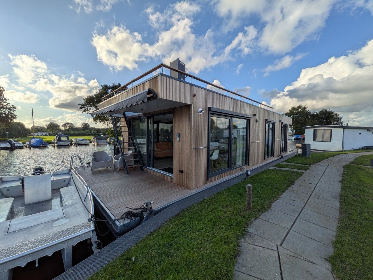 Een moderne woonboot met een dek, zithoek en grote ramen.