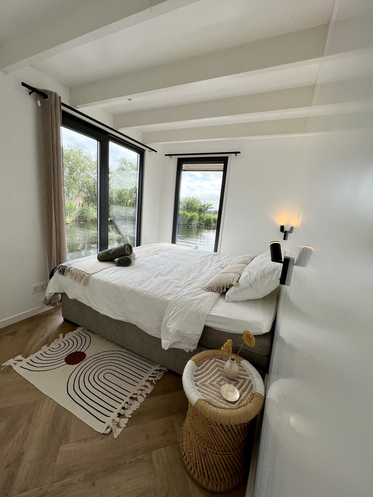 Een slaapkamer met een bed, een raam, een nachtkastje en een vloerkleed.