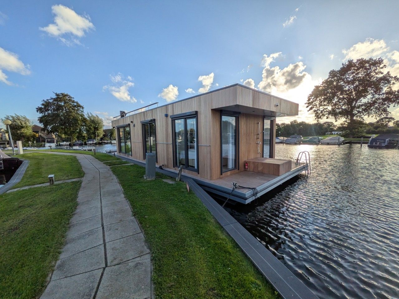 Uma moderna casa flutuante com deck, janelas amplas e uma pequena área externa.