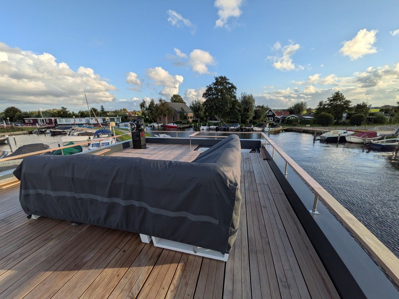 Eine Holzterrasse mit überdachter Sitzgelegenheit mit Blick auf eine Marina und Boote.