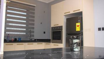A modern kitchen with a built-in oven, a refrigerator, and a window with blinds.