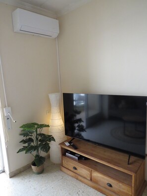 A room with a flat-screen TV on a wooden stand, a potted plant, a wall-mounted air conditioner, and a lamp. - Beachfront Dos Nanitos, right on the beach. Private parking. Pets welcome! (San Pedro del Pinatar)
