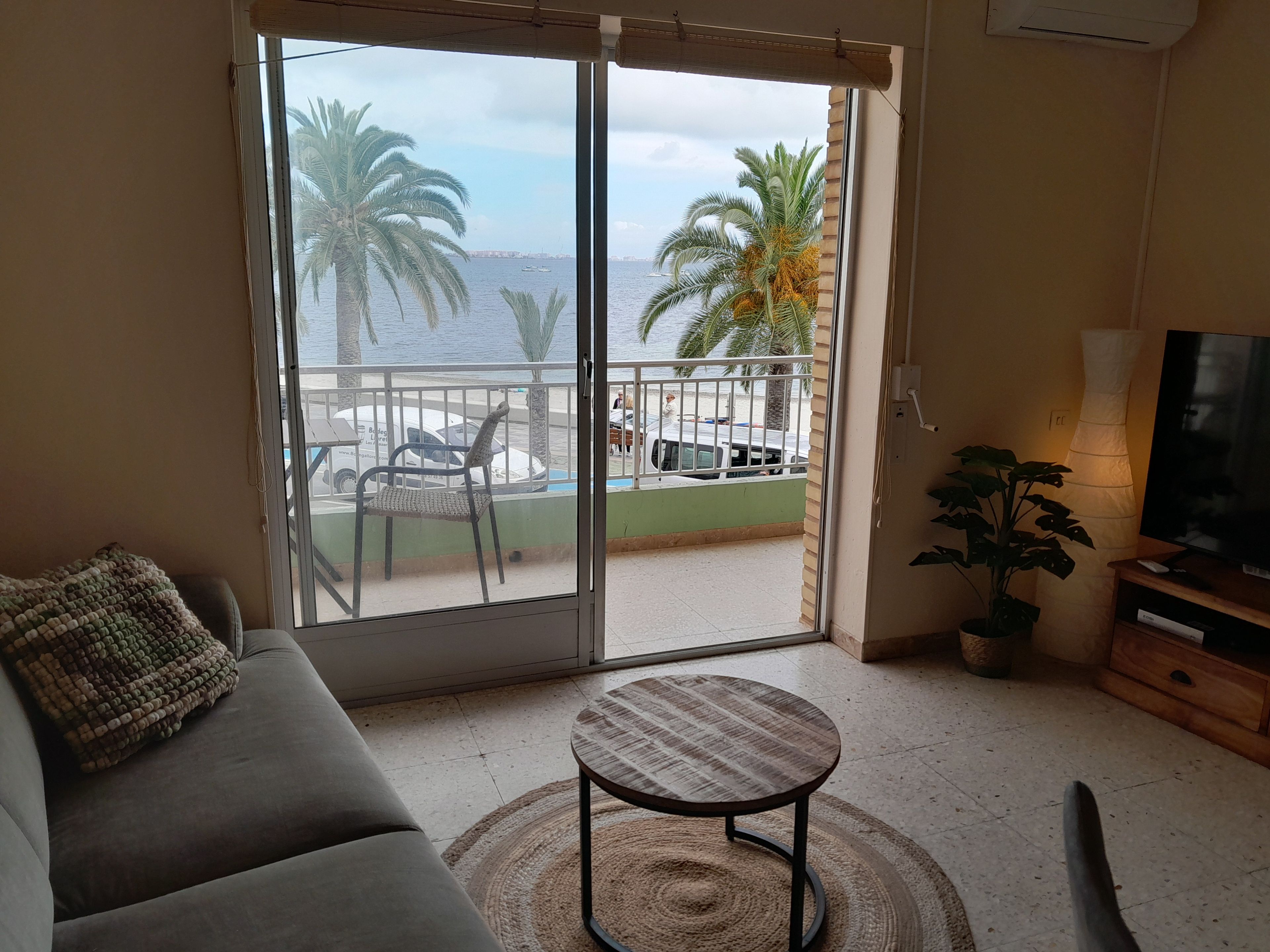 A living room with a sofa, a small round table, a TV, and a view of the sea through a sliding door.