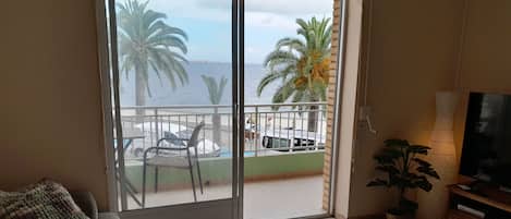 A living room with a sofa, a small round table, a TV, and a view of the sea through a sliding door.