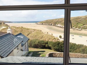 A coastal view from a window overlooking a beach, grassy hills, and a stone wall. - Chy-an-lowena (Newquay)