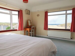 A bedroom with a bed, a desk with a chair, a window with a view of the beach, and a radiator. - Chy-an-lowena (Newquay)