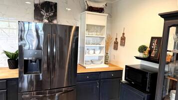 A modern kitchen with a stainless steel refrigerator, a microwave, and a white shelving unit with glassware.