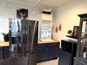 Una cocina moderna con un refrigerador de acero inoxidable, un microondas y una estantería blanca con cristalería.