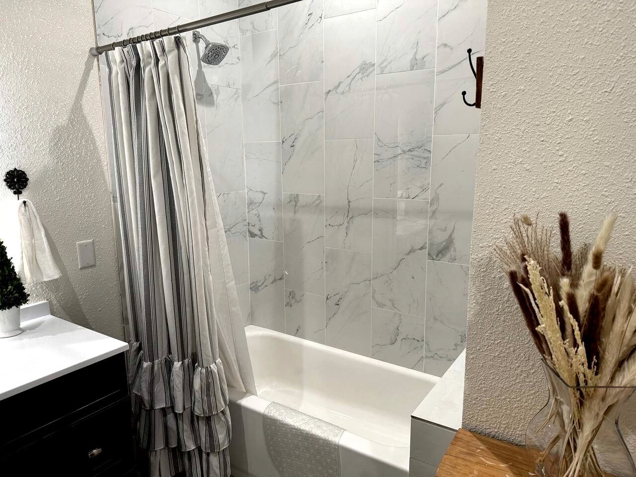 A bathroom with a bathtub, a shower curtain, and a vase with dried plants.